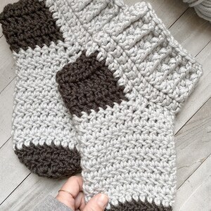 May include: A pair of crocheted slippers with a gray and brown striped pattern. The slippers have a ribbed cuff and a pointed toe.