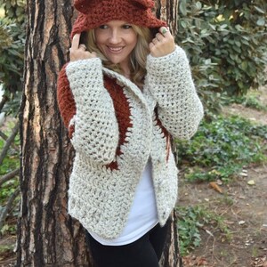 May include: A crocheted cardigan with a fox-shaped hood in brown and white. The cardigan has a white background with brown accents and a brown hood with fox ears.