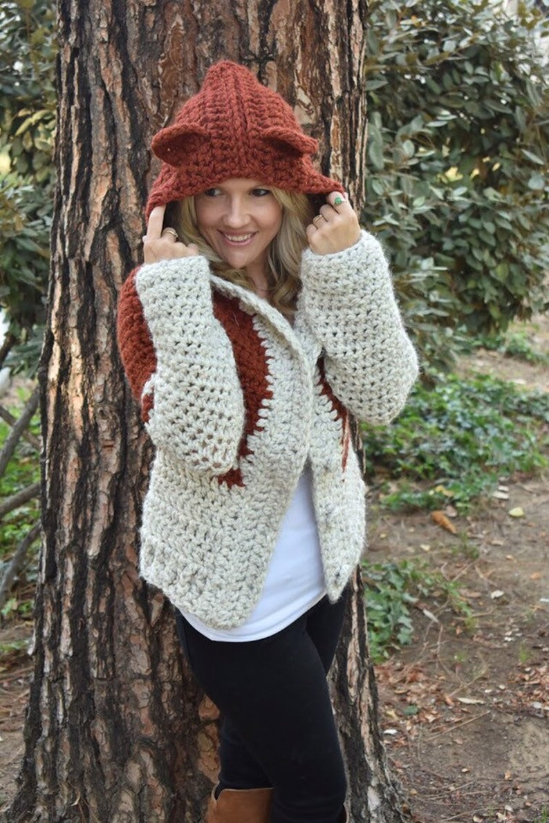 May include: A crocheted cardigan with a fox-shaped hood in brown and white. The cardigan has a white background with brown accents and a brown hood with fox ears.