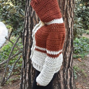 May include: A crocheted hooded sweater with a rust and cream colour pattern. The sweater has a long sleeve and a hood with a pointed tip.