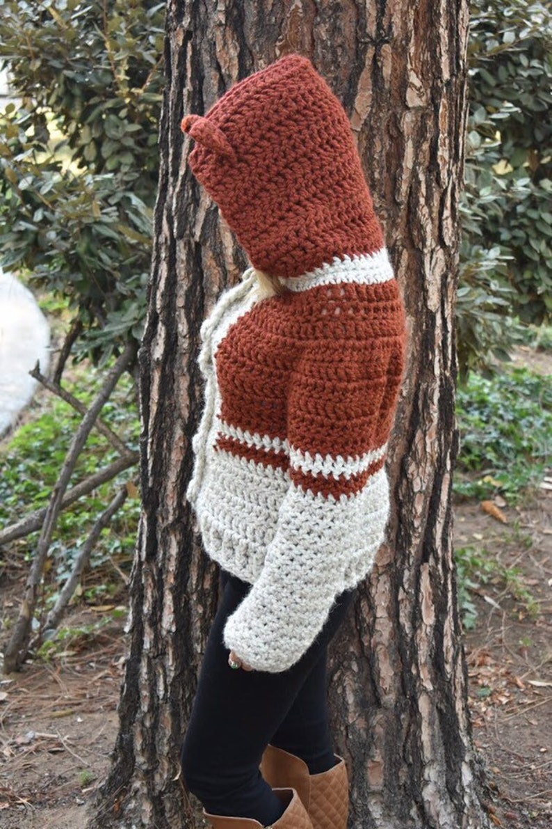 May include: A crocheted hooded sweater with a rust and cream colour pattern. The sweater has a long sleeve and a hood with a pointed tip.