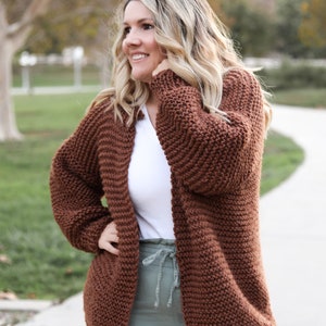 May include: A brown knitted cardigan with a relaxed fit and long sleeves. The cardigan is made of a chunky yarn and has a simple design.