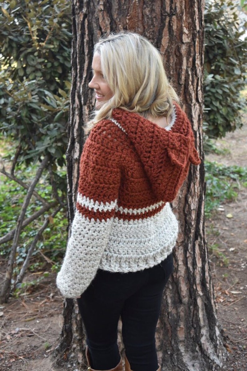 May include: A crocheted hooded sweater with a rust coloured body and white sleeves. The sweater has a white crocheted trim around the hood and sleeves.