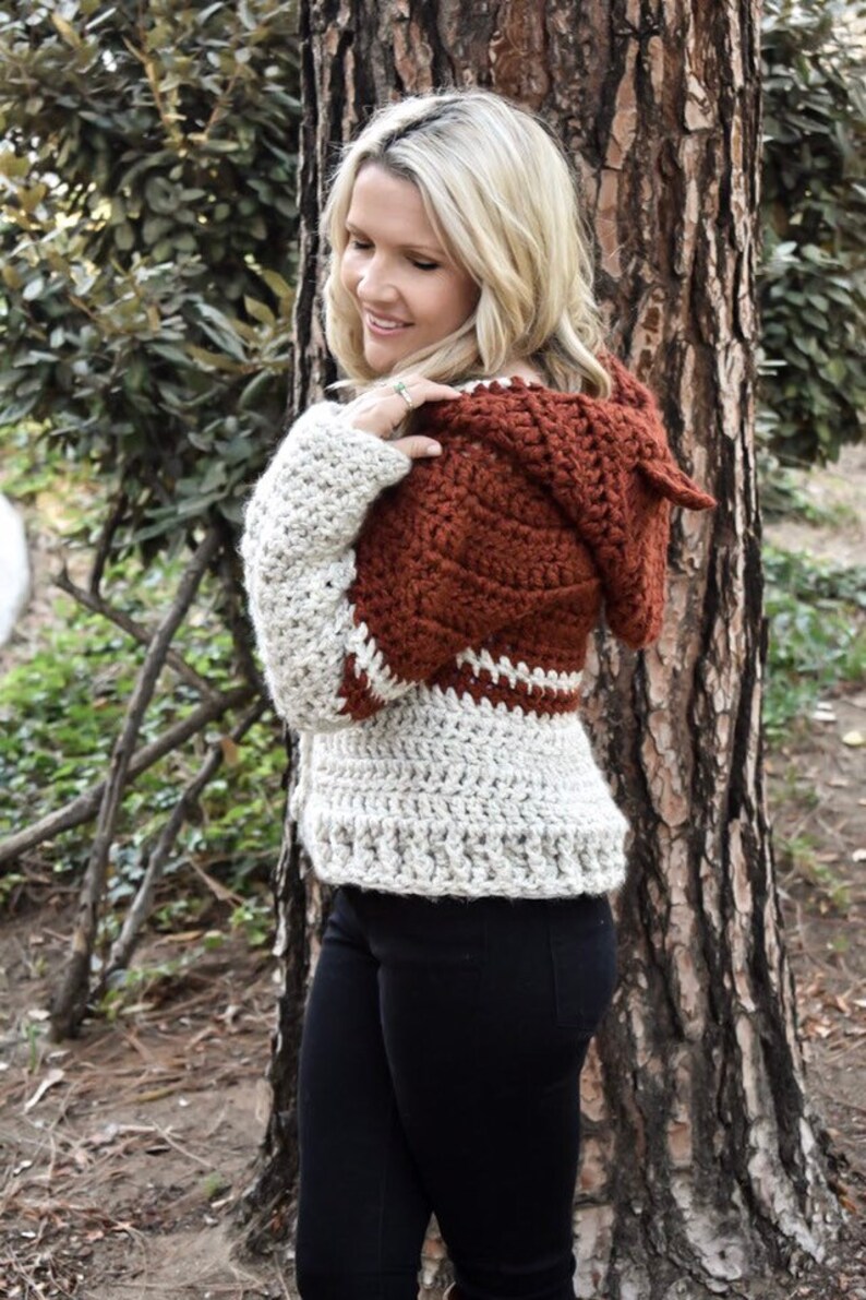 May include: A crocheted hooded sweater in a brown and white colour scheme. The sweater has a loose fit and a relaxed style.