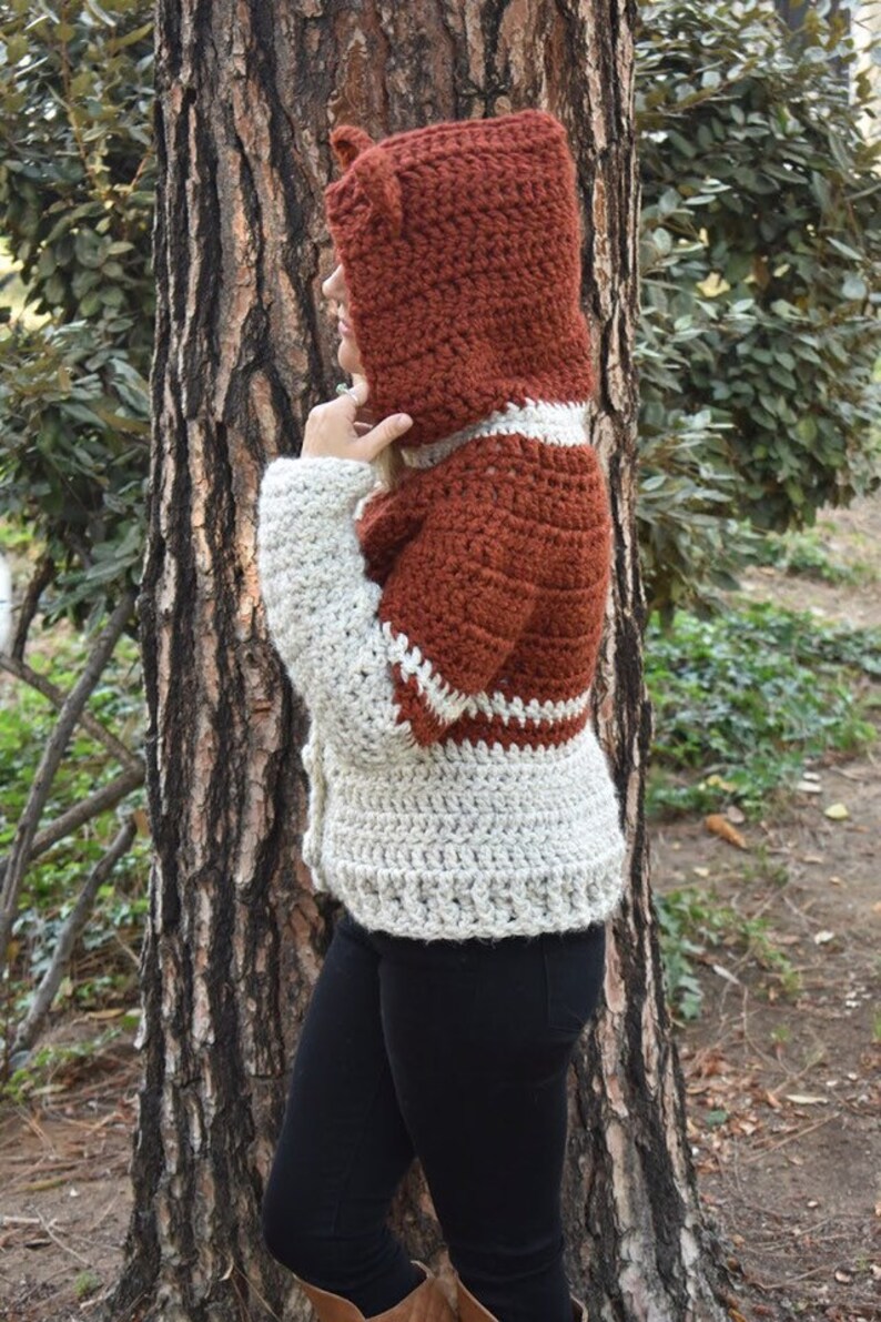 May include: A brown and white crocheted cardigan with a hood and ear flaps. The cardigan has a button closure and a white trim around the edges.