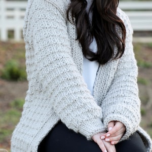 May include: A light gray knitted cardigan with a textured stitch pattern. The cardigan is open in the front and has long sleeves.