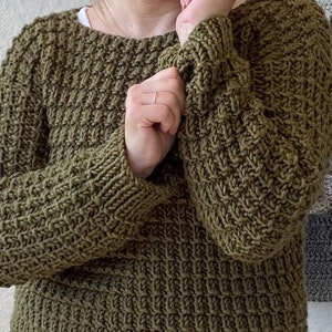 May include: A green knitted sweater with a textured stitch pattern. The sweater has long sleeves and a crew neckline.