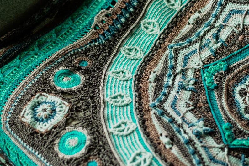 May include: A close-up of a crocheted blanket with a circular design in shades of brown, teal, and green.