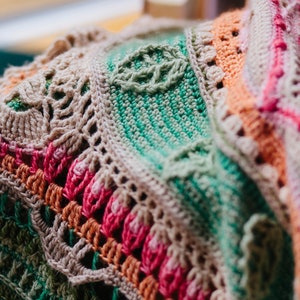 May include: Close-up of a crocheted blanket with a multi-colored pattern. The blanket is made with a variety of stitches and colors, including green, pink, orange, and brown. The blanket is folded in half, and the edges are visible. The text "d'Histoire Naturelle" is visible in the top left corner of the image.