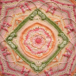 May include: A crocheted mandala with a central flower design in shades of pink, orange, and green. The mandala is surrounded by a border of leaves and flowers.