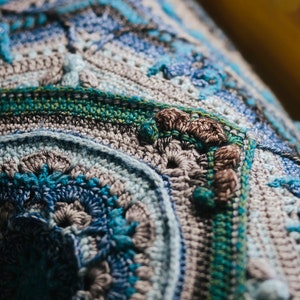 May include: Close-up of a crocheted blanket with a blue, gray, and green color scheme. The blanket has a textured pattern and is made with a variety of stitches. The text "SCHEEPJES CAL 2020 d'Histoire Naturelle" is visible in the bottom right corner.