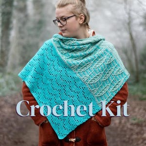 Op de afbeelding: Een driehoekige gehaakte sjaal met een fel turquoise gedeelte met een opengewerkt rasterpatroon en een lichter mintgroen gedeelte met een gestructureerd bladmotief. De tekst "Crochet Kit" staat in het wit over het midden van de sjaal.