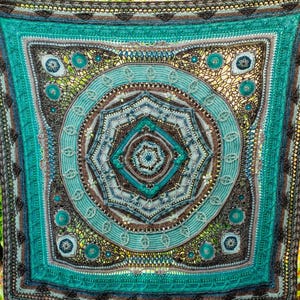 May include: A large, crocheted blanket with a circular mandala design in shades of teal, blue, brown, and gray. The mandala features intricate details and a variety of textures.