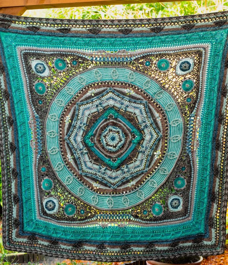 May include: A large, crocheted blanket with a circular mandala design in shades of teal, blue, brown, and gray. The mandala features intricate details and a variety of textures.