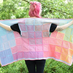 Op de afbeelding: Een kleurrijk gebreid vest met een patchwork-ontwerp met vierkanten in tinten blauw, roze en geel. Het vest heeft een losse, open voorkant en is gemaakt met een textuur-steek.