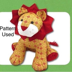 May include: A stuffed lion toy featuring a gold fabric body with a repeating red floral pattern, a white muzzle, and a dark red mane. The text "Pattern Used" is printed on the left side of the lion. The toy has black eyes and a red nose.