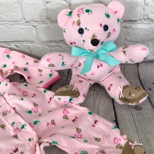 May include: A pink baby onesie with a monkey and house print and a pink teddy bear with a turquoise bow. The teddy bear has brown eyes and a black nose.