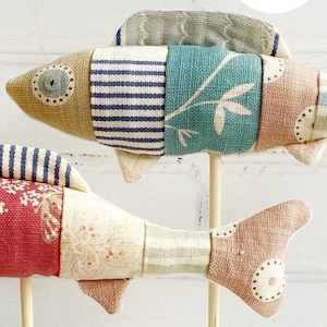 May include: Two colorful patchwork fabric fish ornaments with wooden sticks. The fish are made of different patterned fabrics in shades of blue, green, red, and brown.