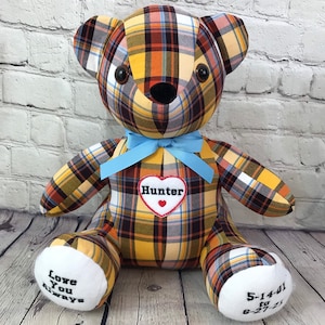 May include: A stuffed teddy bear made from yellow, orange, brown, and blue plaid fabric. It features a light blue ribbon around its neck, a white heart patch with the name Hunter, and white foot pads embroidered with Love You Always and 5-14-01 to 6-27-21.
