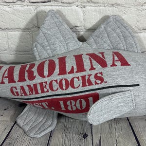 Op de afbeelding: Grijze pluche vis met een rood en wit "Carolina Gamecocks Est. 1801" logo.
