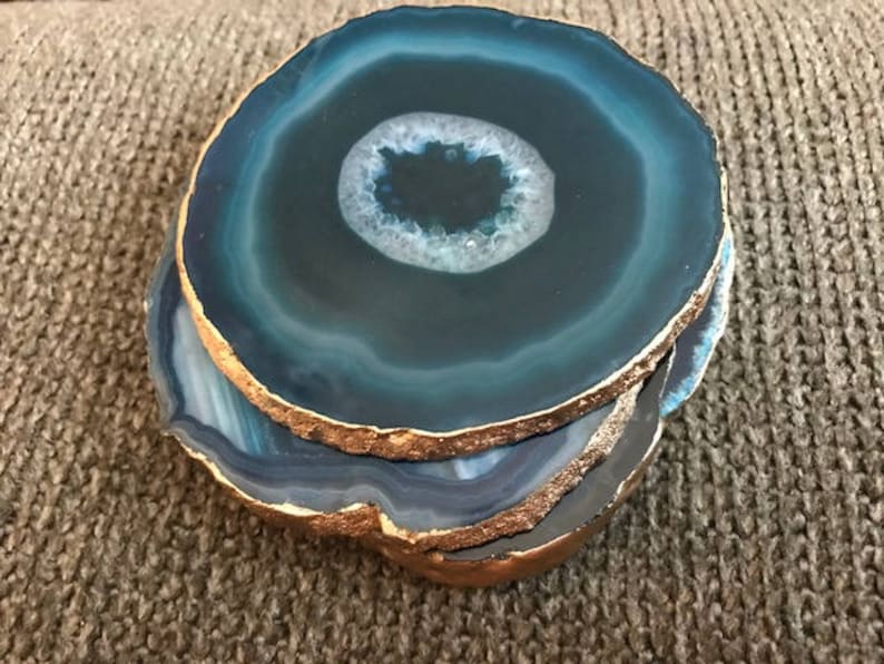 May include: A stack of four blue agate coasters with gold-painted edges. The coasters have a circular shape with a white and blue center, and are stacked on top of each other.