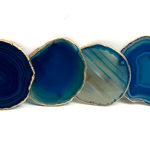 May include: Four blue agate coasters with gold gilded edges are arranged in a row against a white background. The coasters vary in shades of blue, from deep navy to light teal, and have unique natural patterns.