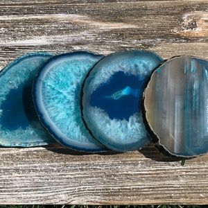 May include: Four agate coasters in shades of blue and white. The coasters are round and have a natural, polished finish.