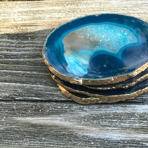 May include: A stack of four agate coasters with a vibrant blue and white interior and gold-painted edges. The coasters are made of natural stone and are a decorative home accessory.
