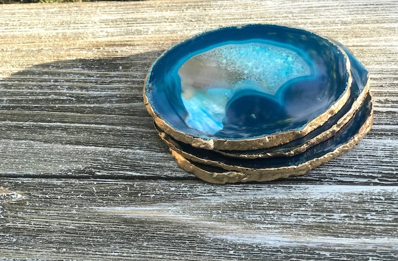 May include: A stack of four agate coasters with a vibrant blue and white interior and gold-painted edges. The coasters are made of natural stone and are a decorative home accessory.