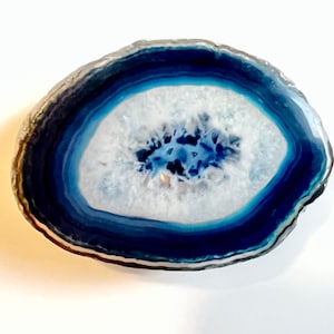 May include: A blue agate slice with white and blue banding. The agate has a natural, organic shape and a smooth, polished surface.