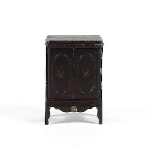 Peut inclure: Un petit meuble en bois brun foncé à deux portes et des détails ornés. Le meuble est de forme rectangulaire avec un dessus plat et repose sur quatre pieds incurvés. Les portes ont des boutons ronds.