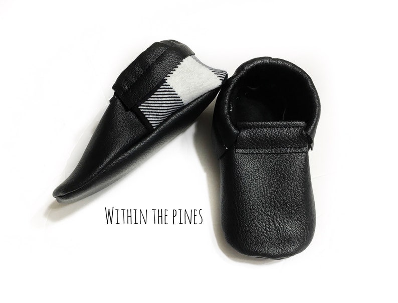 Puede incluir: Un par de mocasines de beb&eacute; de cuero negro con forro de cuadros blanco y negro. Los mocasines son suaves y flexibles, perfectos para pies peque&ntilde;os.