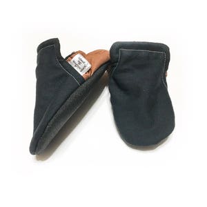 May include: A pair of black baby moccasins with a brown leather sole. The moccasins have a label that says "Wild & Free" on them.