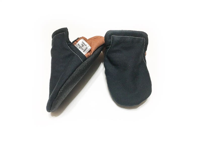 May include: A pair of black baby moccasins with a brown leather sole. The moccasins have a label that says "Wild & Free" on them.