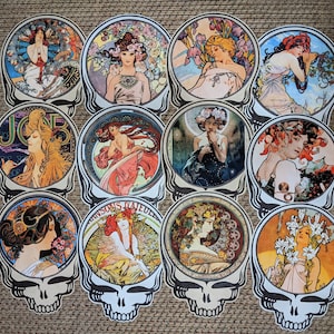 May include: A collection of twelve decorative stickers featuring Art Nouveau-style illustrations of women surrounded by flowers and ornate details. Each design is set within a circular frame and mounted on a skull-shaped background with a black and white color scheme.