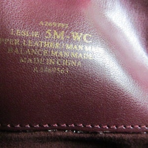 Puede incluir: Primer plano de un bolso de cuero burdeos con letras doradas que dicen "Leslie 5M-WC Upper Leather Made in Italy Balance Leather Made in Italy All Ingredients Made in Italy".