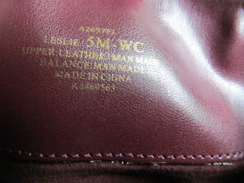 Puede incluir: Primer plano de un bolso de cuero burdeos con letras doradas que dicen "Leslie 5M-WC Upper Leather Made in Italy Balance Leather Made in Italy All Ingredients Made in Italy".
