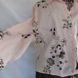 May include: A long-sleeved, light pink button-down shirt with a brown floral print. The shirt has a relaxed fit and a slightly gathered waist.