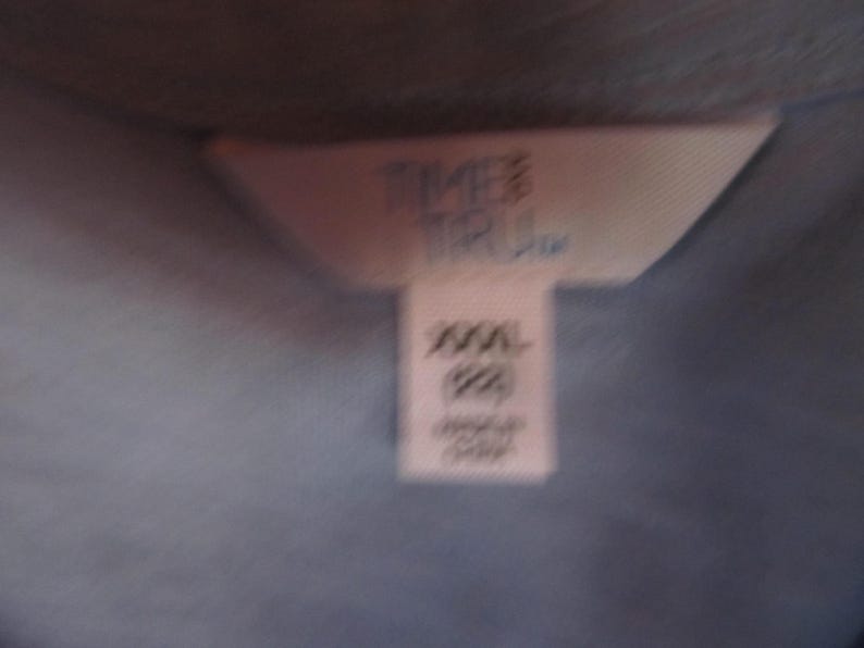 Pu&ograve; includere: Un'etichetta bianca con il testo "Timberland" e "XXL" su di essa. L'etichetta &egrave; attaccata a un capo di abbigliamento blu chiaro.