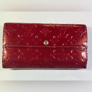 May include: A red leather wallet with a gold snap closure and a Louis Vuitton monogram pattern.