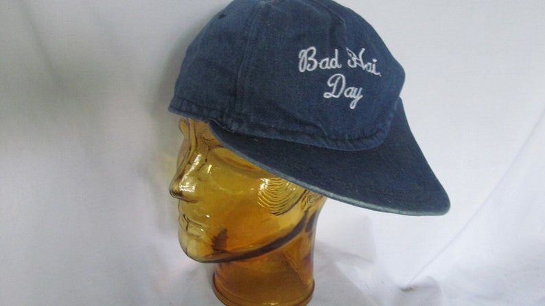 May include: A blue denim baseball cap with white embroidery that reads "Bad Hair Day".