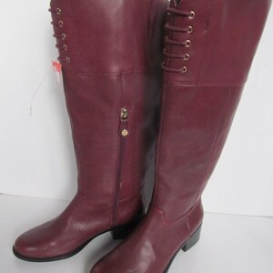 Puede incluir: Un par de botas de cuero burdeos de ca&ntilde;a alta con detalles de cordones en la parte posterior de las botas.