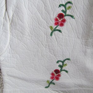 Puede incluir: Guantes de cuero blanco con dise&ntilde;os florales bordados en rojo y verde.