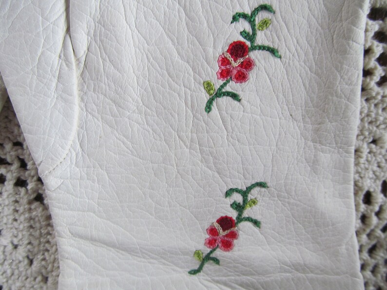 Puede incluir: Guantes de cuero blanco con dise&ntilde;os florales bordados en rojo y verde.