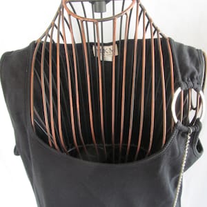 May include: Black sleeveless top with a silver ring detail and chain. The top has a scoop neck and is made of a soft, stretchy fabric.