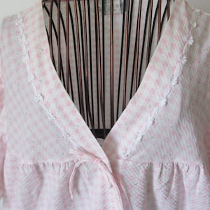 May include: A pink and white gingham robe with white lace trim around the neckline and sleeves. The robe has a tie at the waist.