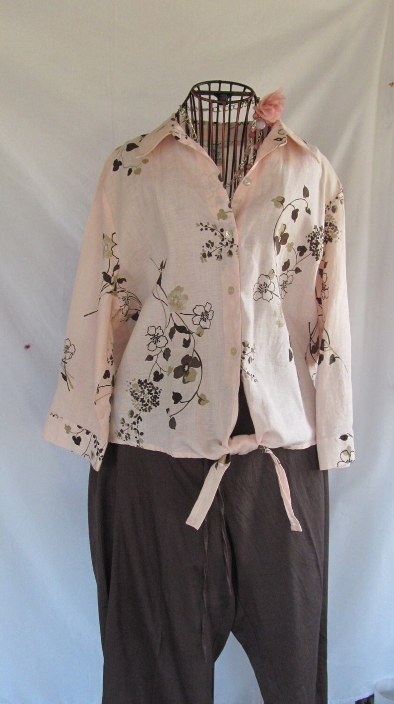 May include: A pink and brown floral print button-up shirt with long sleeves and a tie at the waist. The shirt is paired with brown trousers.