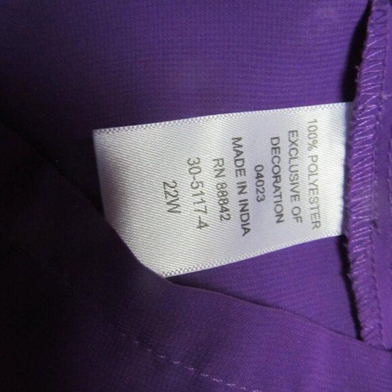 May include: A close-up shot of a purple garment with a white label. The label states "100% Polyester Exclusive of Decoration" and includes details such as "Made in India", "RN 88842", and size "22W".