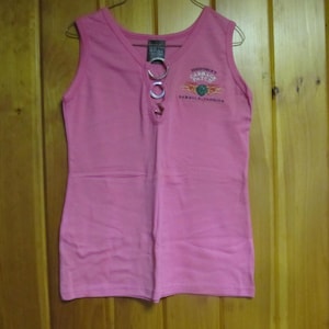 May include: Pink sleeveless tank top with a silver chain detail and the text "GARBAGE PATCH" and "SANTA CRUZ, CALIFORNIA".