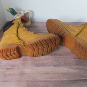 Op de afbeelding: Een paar bruine leren werkschoenen met zwarte accenten en een dikke rubberen zool. De schoenen zijn gedragen en hebben een vintage uitstraling.